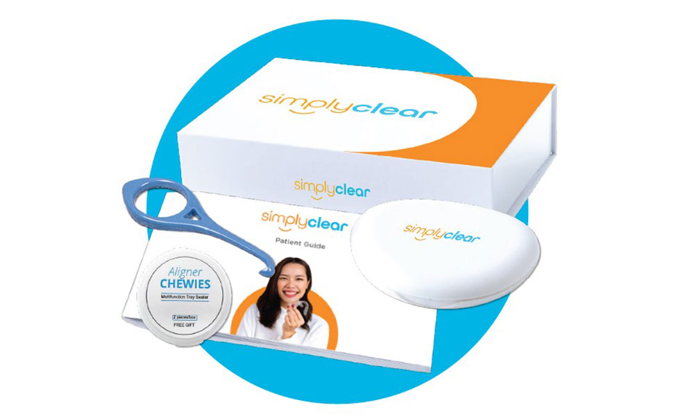 A SimplyClear aligner kit displayed on a blue circle background, featuring a branded box, aligner case, aligner chewie container with a smiling woman‚Äôs photo, an aligner removal tool, and a patient guide booklet.